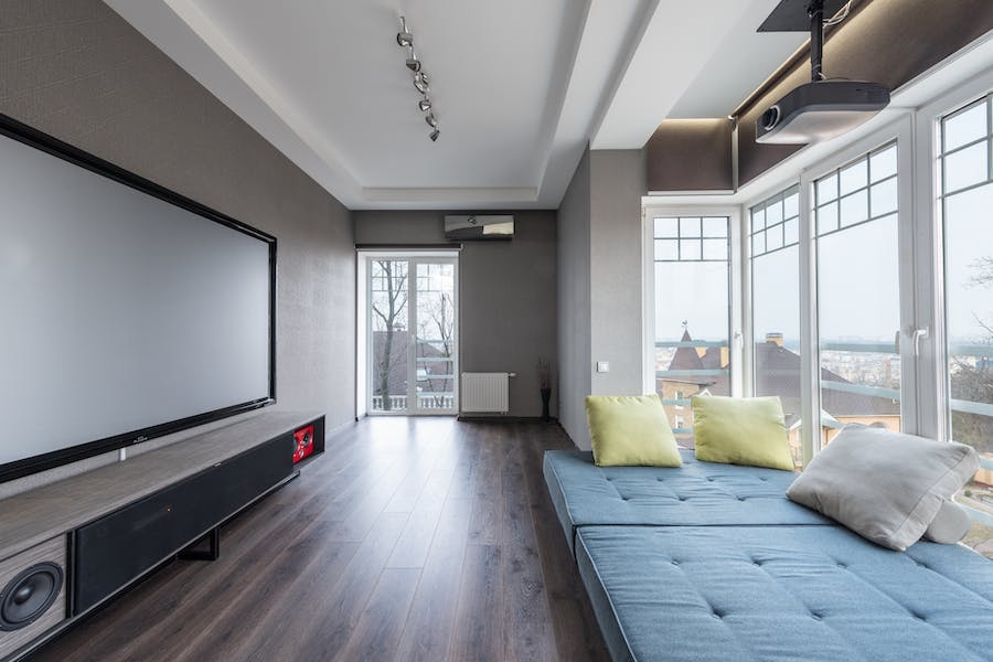A cozy home media room with large windows and a huge projector set up on the wall.
